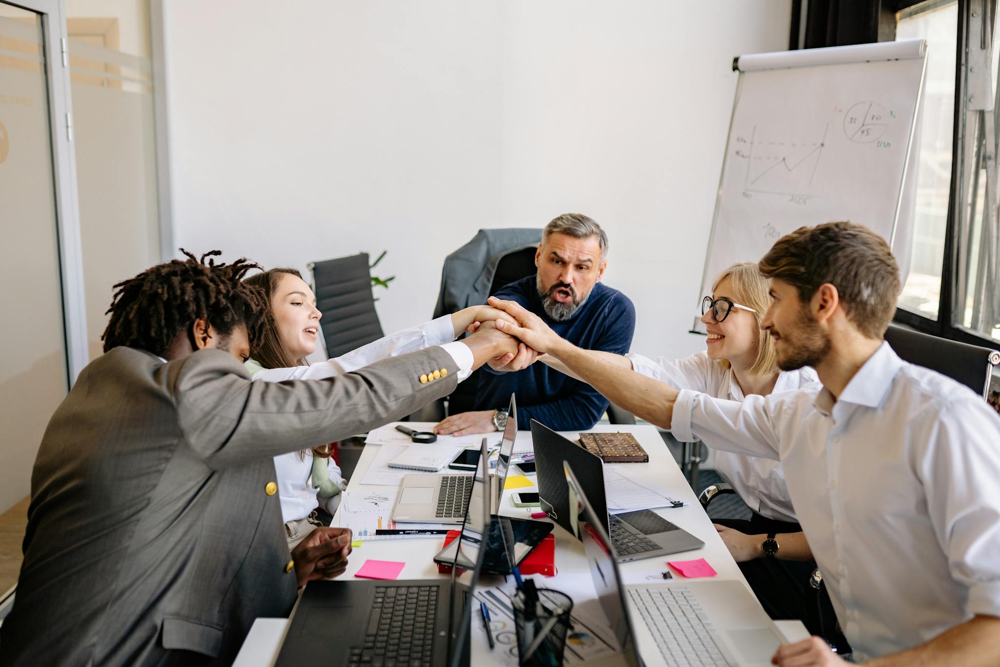 A diverse group of colleagues unites in a team huddle at a modern office meeting.